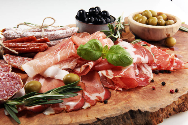 Marmeren snijplank met ham, spek, salami en worstjes op houten achtergrond. Vlees schotel hapjes en olijven - Foto, afbeelding