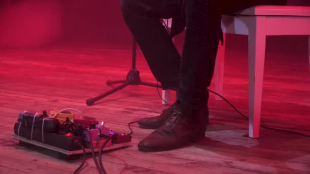 Гитарист меняет звуковой эффект на педальную доску с ногой на сцене во время музыкального шоу с красным светом и дымом на заднем плане
. - Кадры, видео