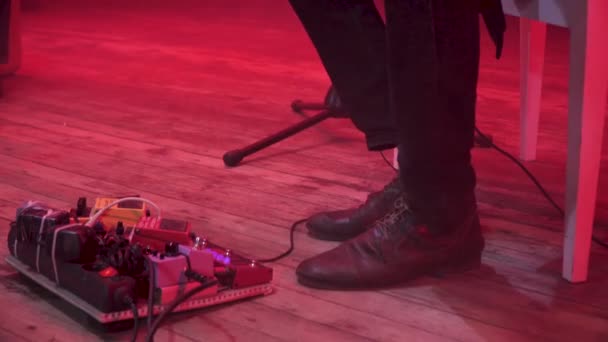 ギタリストが赤色光と背景の煙で音楽ショーの間に舞台の床に足でエフェクト ペダル ボードのサウンド効果を変更します。. - 映像、動画