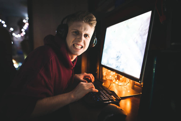 Porträt eines emotionalen Teenagers, spielt Videospiele auf einem Heimcomputer und blickt auf einen bösen Blick in die Kamera. wütender Spieler spielt nachts Online-Videospiele, zu Hause in einem gemütlichen Raum. Spielkonzept - Foto, Bild