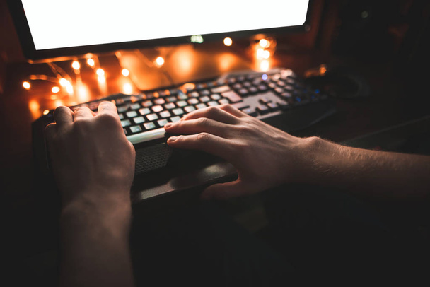 Руки молодого игрока, играющего ночью в видеоигры на компьютере, руках и клавиатуре крупным планом. Клавиатура с подсветкой и рукопожатным текстом. Фон. Киберспорт. Руки на клавиатуру
 - Фото, изображение