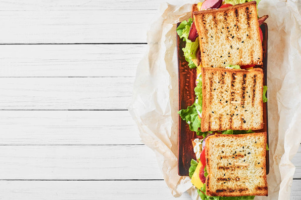Three sandwiches with ham, lettuce and fresh vegetables on a white background, top view with copy space - Foto, Imagem