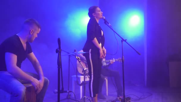 Muziekband uitvoeren op het podium in blauwe concert licht en rook in de achtergrond. Drie muzikanten - meisje zanger, drummer en gitarist uitvoeren muziek tijdens de show. - Video