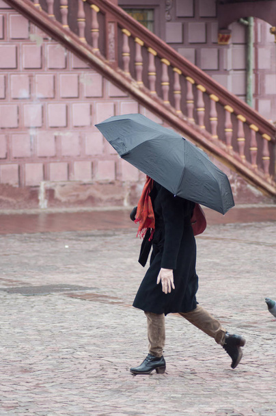 Πορτρέτο γυναίκας με ομπρέλα διασχίζει ένα τετράγωνο πλακόστρωτα της πόλης - Φωτογραφία, εικόνα