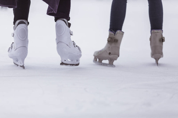 close-up of womens legs on skates in winter on an open skating rink, place for text. The ice skates of two friends skating together on a winter afternoon. Winter time, outdoor activities - concept - Photo, image