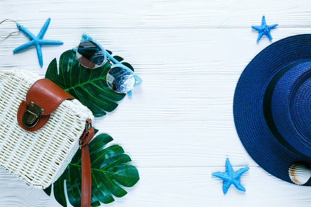 weiße Öko-Rattan-Tasche tropischen Dschungel Palme Monstera Blätter Seesterne Schale und eine Frau den blauen Hut auf weißem Holztisch. Sommer-Hintergrund, Urlaub, Reise kreatives Wohnungslegekonzept - Foto, Bild