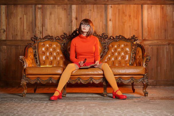 Nettes Mädchen mit Brille in orangefarbener Kleidung ist eine gute Studentin und ein Nerd, sie liest gerne allein zu Hause auf dem Sofa Buch - Foto, Bild
