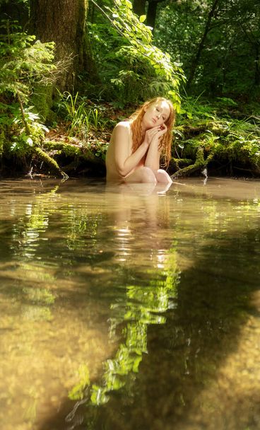 nuori seksikäs punatukkainen nainen istuu kesävalossa puron joessa rannalla tukee päätä käsissään ja unelmoi rakkaudesta
 - Valokuva, kuva