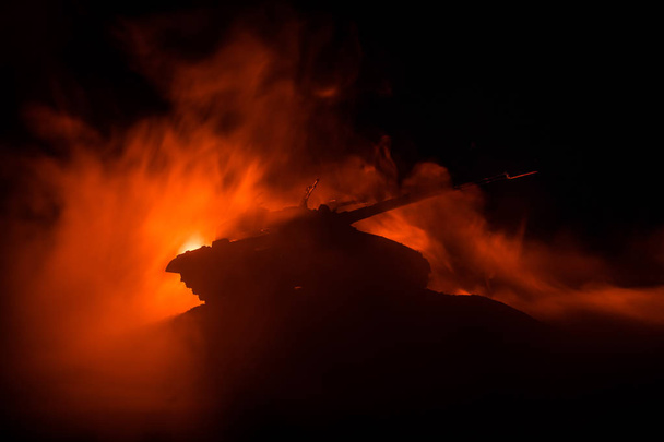 Concept van de oorlog. Gepantserde Tank silhouet onder mistige brand nachthemel. Aanval scène. Speelgoed decoratie. Selectieve aandacht - Foto, afbeelding