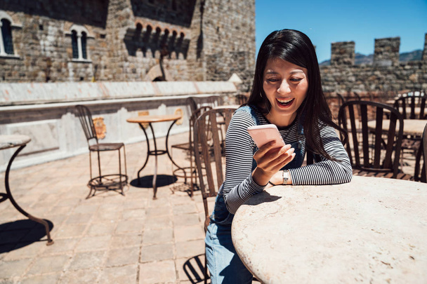 girl sitting on the wooden historical chair rooftop outdoor cafe in the old medieval castle. young asian woman travel love history trip in europe. lady searching online guide book information. - Photo, image