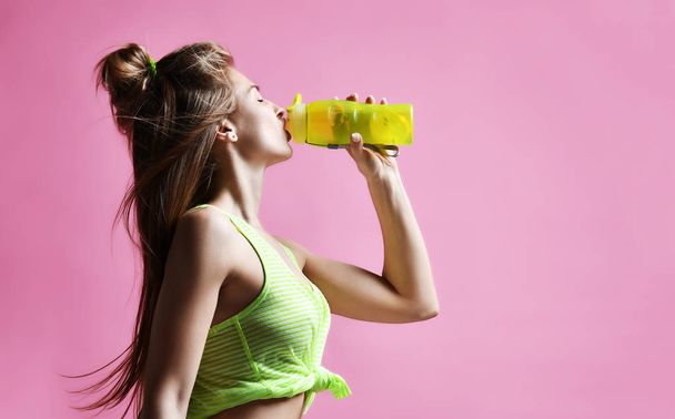 junge Sportlerin hält Trinkwassersportflasche auf rosa - Foto, Bild