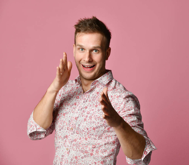 Young happy smiling man in shirt pointing fingers hands up on pink  - Фото, зображення