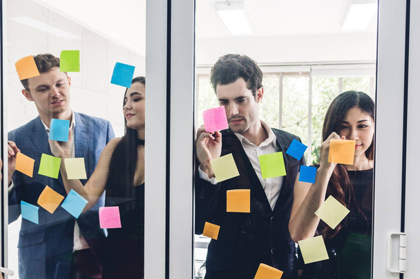 Group of casual business people planning and brainstorm writing over the project with stickers note on glass window at modern office.Teamwork concept - Photo, Image
