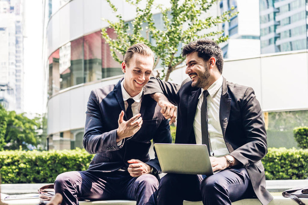 Bild zwei Geschäftspartner im schwarzen eleganten Anzug im Gespräch und bei der Diskussion einer neuen Strategie mit Laptop-Computer bei city.business und Gründungsidee Konzept - Foto, Bild