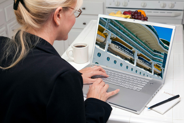 Femme dans la cuisine en utilisant un ordinateur portable avec navire de croisière à l'écran
 - Photo, image