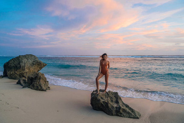 Esbelta chica caucásica en traje de baño se encuentra en la playa del paraíso en el fondo de la hermosa puesta de sol
 - Foto, Imagen