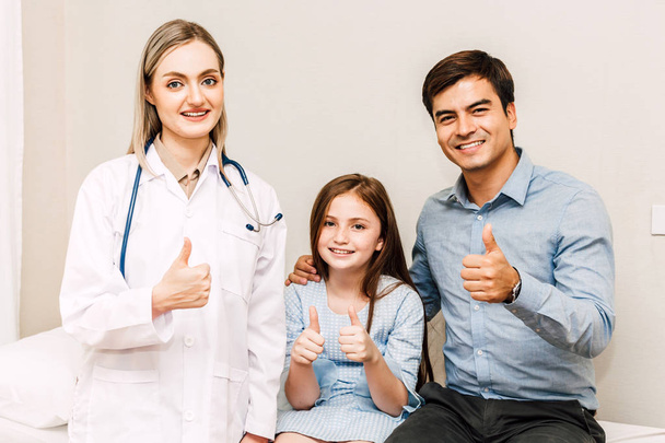 Arzt blickt in die Kamera, während junger Familienvater und kleines Mädchen im Hintergrund zusammen sind - Foto, Bild