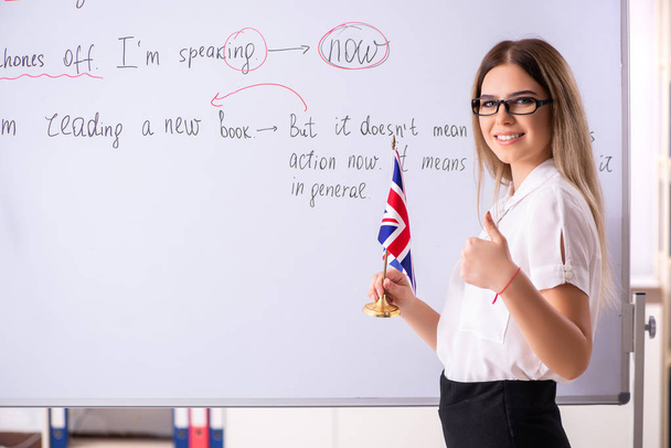 Молодая учительница английского языка стоит перед школьной доской
    - Фото, изображение