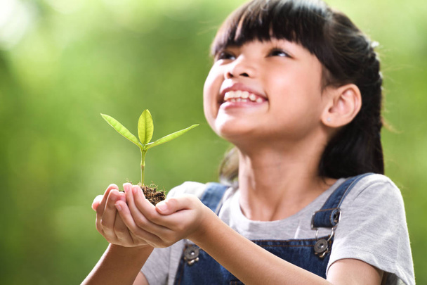 ein Mädchen hält eine junge Pflanze in ihren Händen mit der Hoffnung auf eine gute Umwelt, selektiver Fokus auf Pflanzen - Foto, Bild