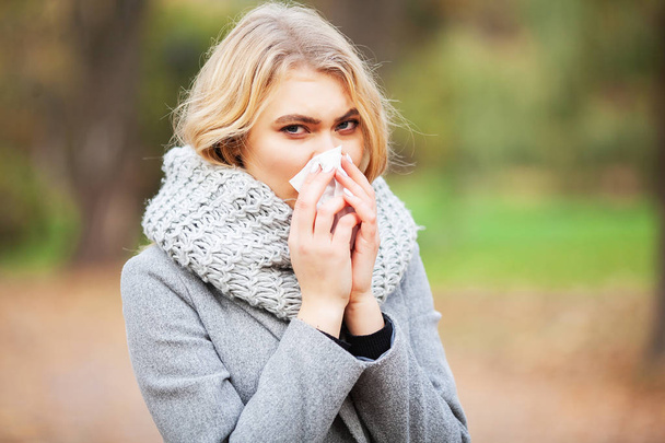 Young woman blowing her nose on the park. Woman portrait outdoor sneezing because cold and flu - Foto, afbeelding