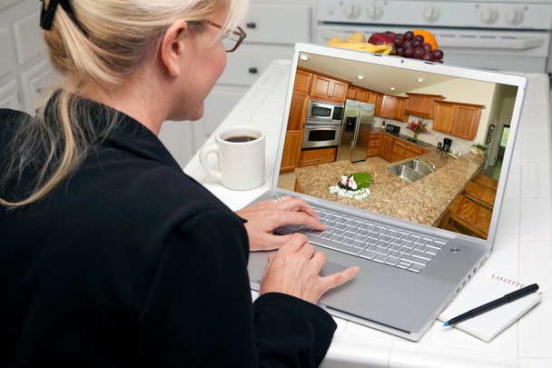 Mujer en la cocina usando el ordenador portátil con el interior de la cocina en pantalla
 - Foto, Imagen
