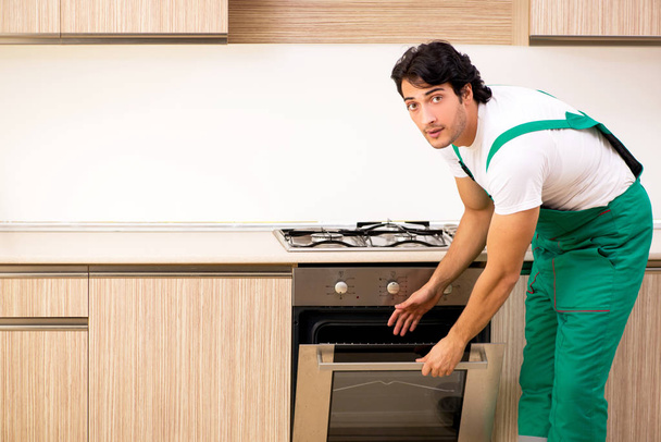 Genç müteahhit mutfakta fırın onarıyor.  - Fotoğraf, Görsel