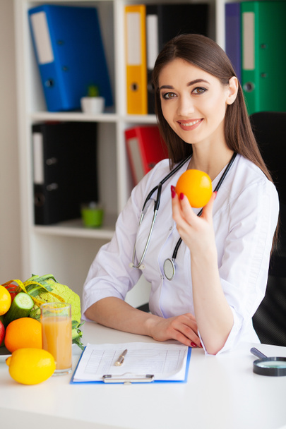 La santé. Docteur diétologue tient dans les mains fraîches orange. Une nutrition saine. Légumes et fruits frais sur la table. Joyeux Docteur dans la Salle Lumière. Haute résolution
 - Photo, image