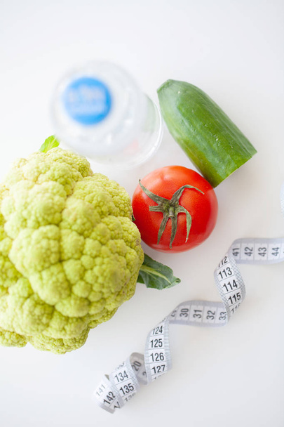 Диета. Концепция здорового питания. Сбалансированная диета с овощами. Свежие зеленые овощи, измерительная лента на белом фоне. Крупный план
 - Фото, изображение