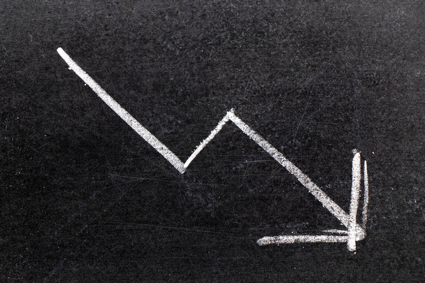 Craie blanche dessin à la main en forme de flèche vers le bas sur fond de tableau noir (Concept de déclin des stocks, tendance à la baisse des entreprises, économie) - Photo, image