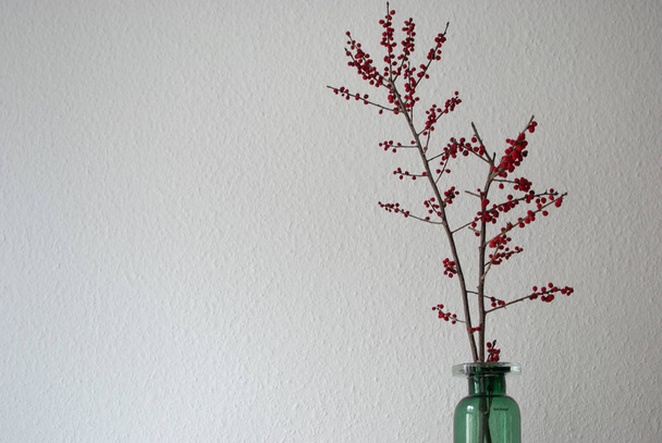 Beyaz duvar arka plan üzerinde winterberry dalları ile yeşil vazo - Fotoğraf, Görsel