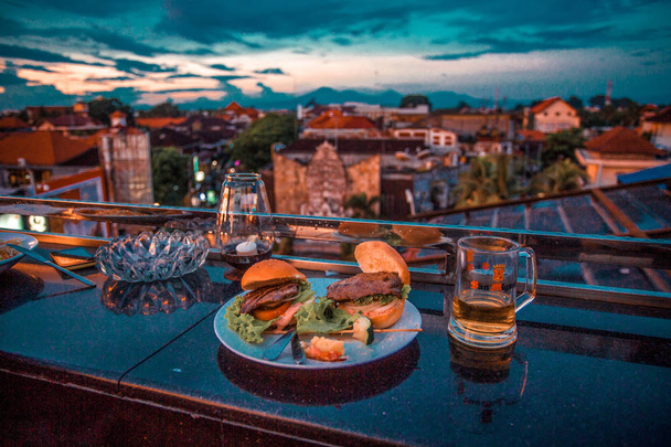 два бургера и бокал пива с видом на город
 - Фото, изображение