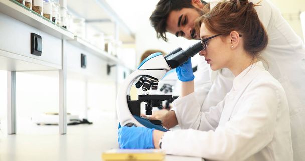 Young female scientist looking through microscope in laboratory - Photo, image