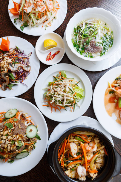 Exotic Vietnamese food restaurant menu close up.Traditional Asian dish served on white plate.Big dinner menu top view.Fresh vegetables salad,fried shrimps & pho bo - Valokuva, kuva