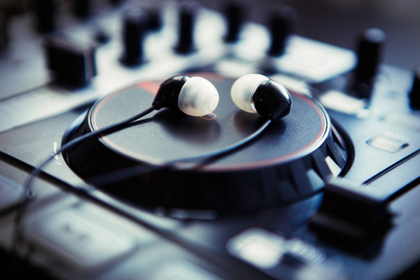 Small black in ear headphones on professional sound mixing midi controller. Hey DJ play the music loud! - Fotó, kép
