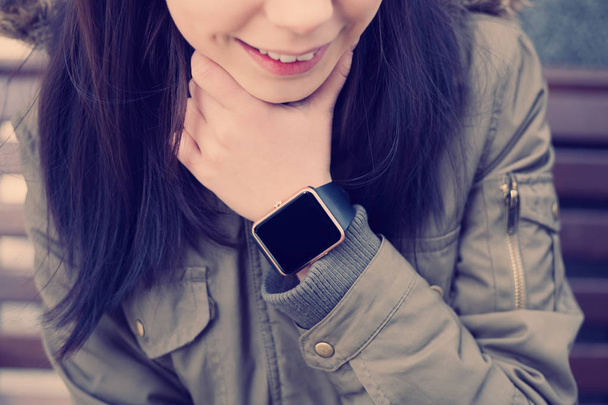 Smiling young chick in parka weating smart watch. This new gadget lets you always stay connected to internet and social media networks from anywhere you want. - 写真・画像
