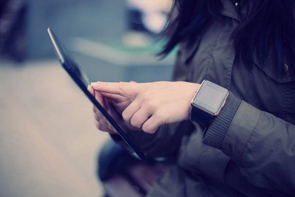 Mulher usando tablet pc enquanto vestindo relógio inteligente em seu pulso. Este novo dispositivo permite que você fique sempre conectado à internet e redes de mídia social de qualquer lugar que você quiser
. - Foto, Imagem