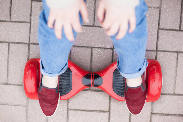 Close up on feet of a gir in marsala shoes riding on a modern red electric mini segway or hover board scooter. Trending new transportation technology that is so much fun and easy to ride and produces no air pollution to the atmosphere. - 写真・画像