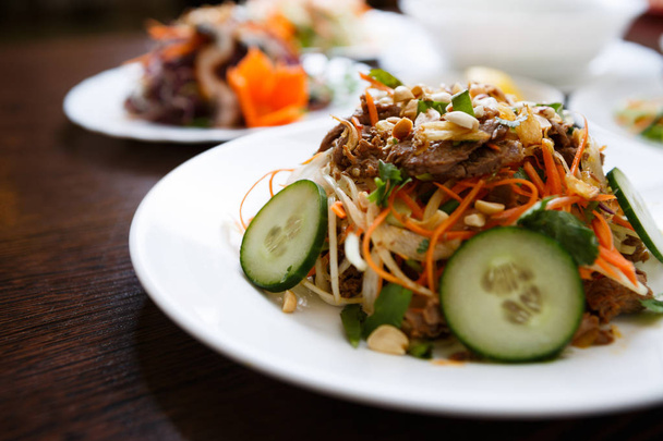 Eat tasty Asian salad with beef meat,fresh cucumber & Chinese carrot with melted nuts topping.Try exotic snack in Vietnamese restaurant with traditional food.Close up,focus on salad. - Foto, Imagen