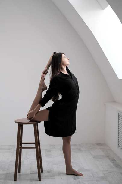 Una joven bailarina vestida de negro se estira por la ventana. Salón Blanco, la clase trabajadora, asanas de yoga
. - Foto, imagen
