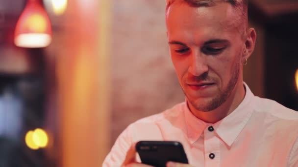Young happy man using smartphone at cozy cafe at evening time. Communication, business, travel, dating concept. - Imágenes, Vídeo