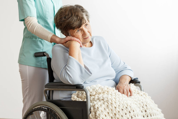 Nurse supporting sad disabled elderly woman in the wheelchair - Photo, image