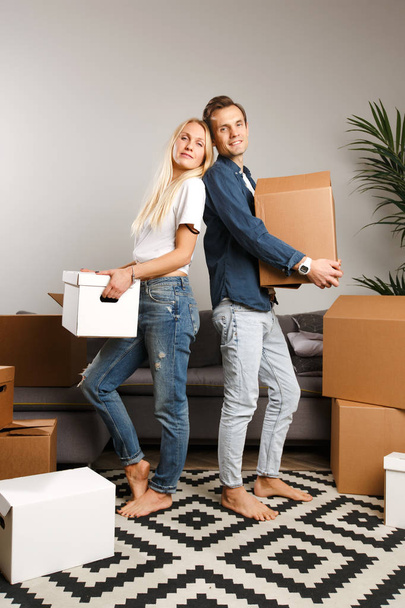 Photo of happy couple standing among cardboard boxes - Фото, изображение