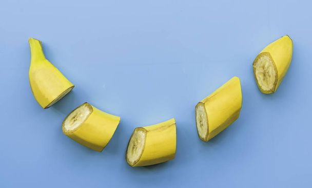 Cut banana slices on blue background flat lay top view. Minimalist concept. Creative fruit concept - Foto, Bild