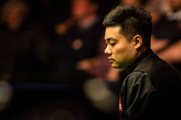 Ding Junhui van China beschouwt een schot aan Zhou Yuelong van China in de eerste fase van hun eerste ronde gelijke tijdens 2017 Betfred World Snooker Championship bij het theater van de smeltkroes in Sheffield, het UK, 17 april 2017. - Foto, afbeelding