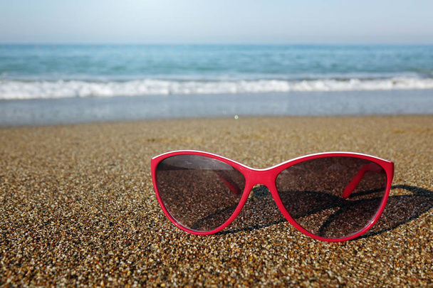 Óculos de sol vermelhos na areia na praia, época de férias
 - Foto, Imagem