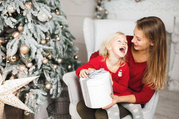 Merry Christmas and Happy Holidays. Cheerful mom and her cute daughter girl exchanging gifts - Foto, Imagen