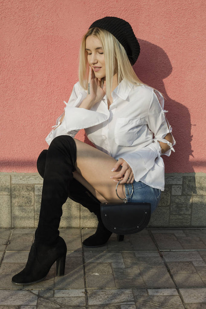Portrait of stylish young woman in white shirt and knee high boots sitting on street - Foto, Bild