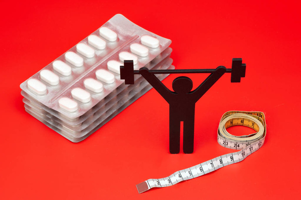 pictograma de levantamento de peso com pílulas e fita métrica, fundo vermelho
 - Foto, Imagem