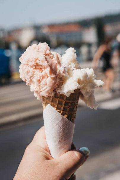 Барвисте морозиво у вафельному конусі, що тримається в руці жінки, розмите місто на фоні
. - Фото, зображення