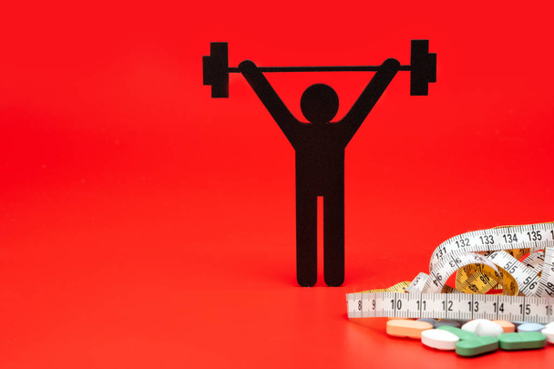 Gewichtheben-Piktogramm mit Pillen und Maßband, roter Hintergrund - Foto, Bild